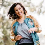 Glückliche Frau trägt eine blaugrüne und goldene Bomberjacke