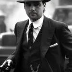 Ein Mann in einem Gangsteranzug aus den 1920er Jahren hält eine Pistole.
