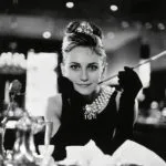 Audrey Hepburn, Frühstück bei Tiffany, ikonisches schwarzes Kleid, Perlenkette, Zigarettenspitze.