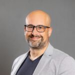 Lächelnder Glatzkopf mit Brille und grauem Blazer