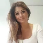 Frau mit langen braunen Haaren und weißem Oberteil lächelt.